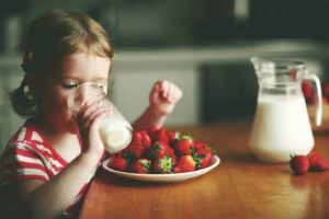Young girl enjoying a glass of lactose free milk and strawberries