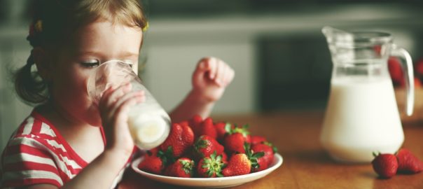 Young girl enjoying a glass of lactose free milk and strawberries