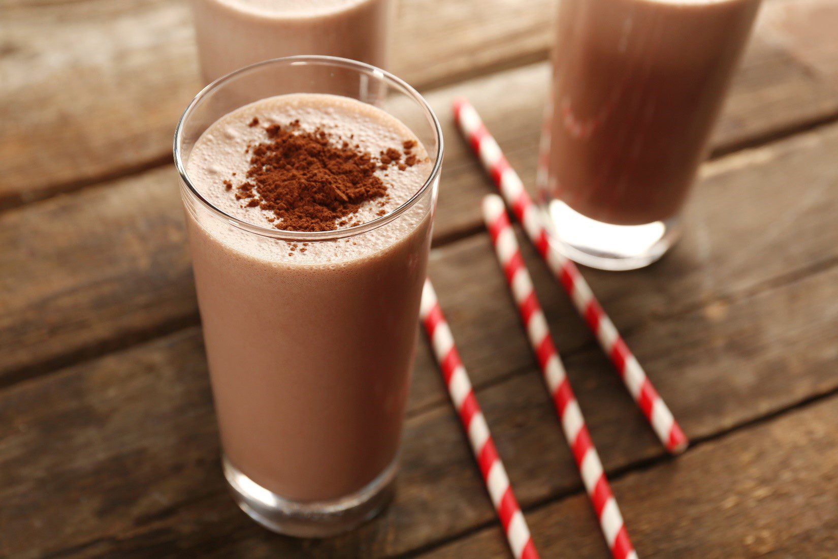 Chocolate lactose free milkshake in glass with cocoa and straws.
