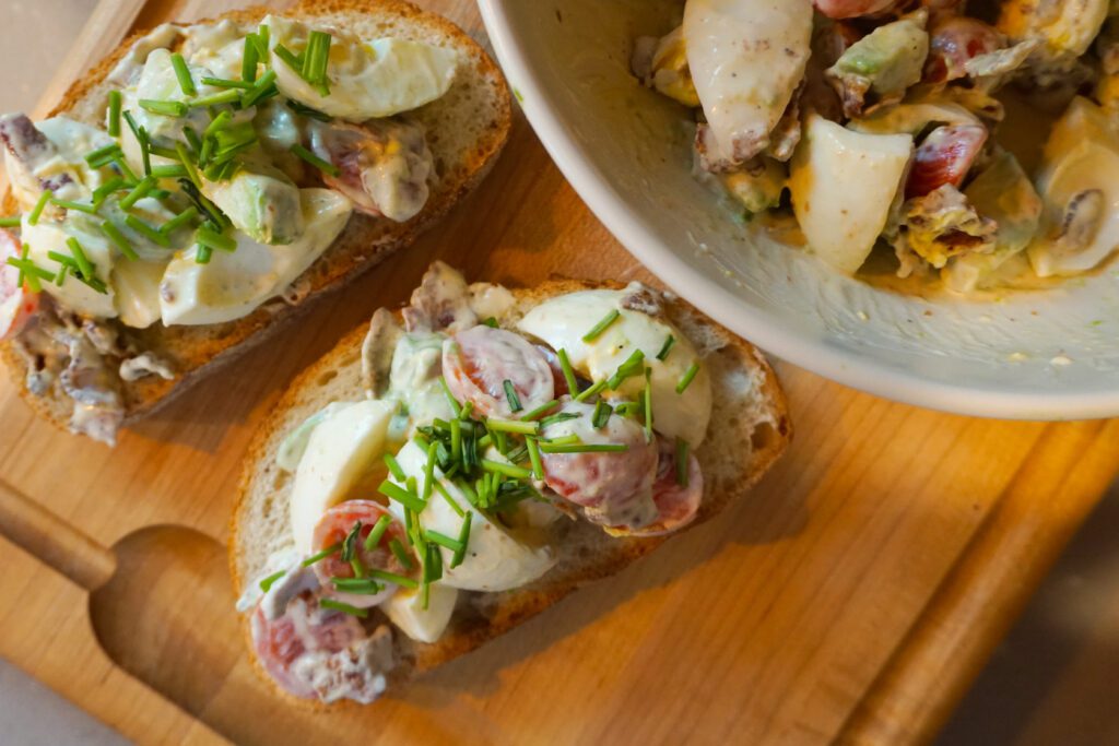 cobb egg salad on sourdough bread open face sandwich on wooden cutting board