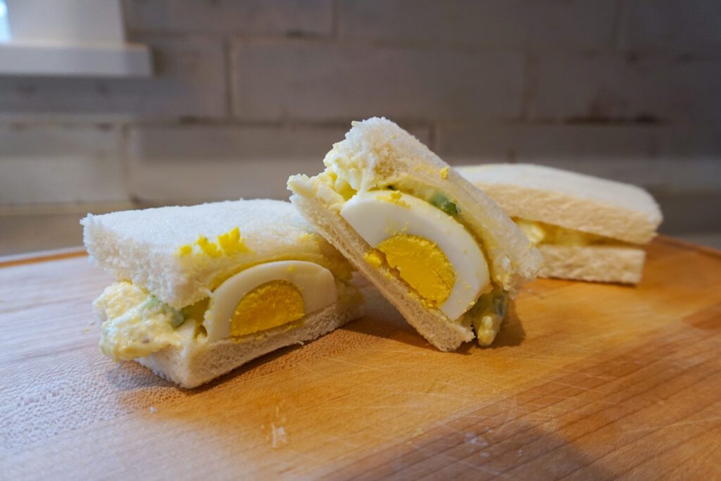 Japanese egg salad sandwiches with hard boiled egg cut in half on wooden cutting board