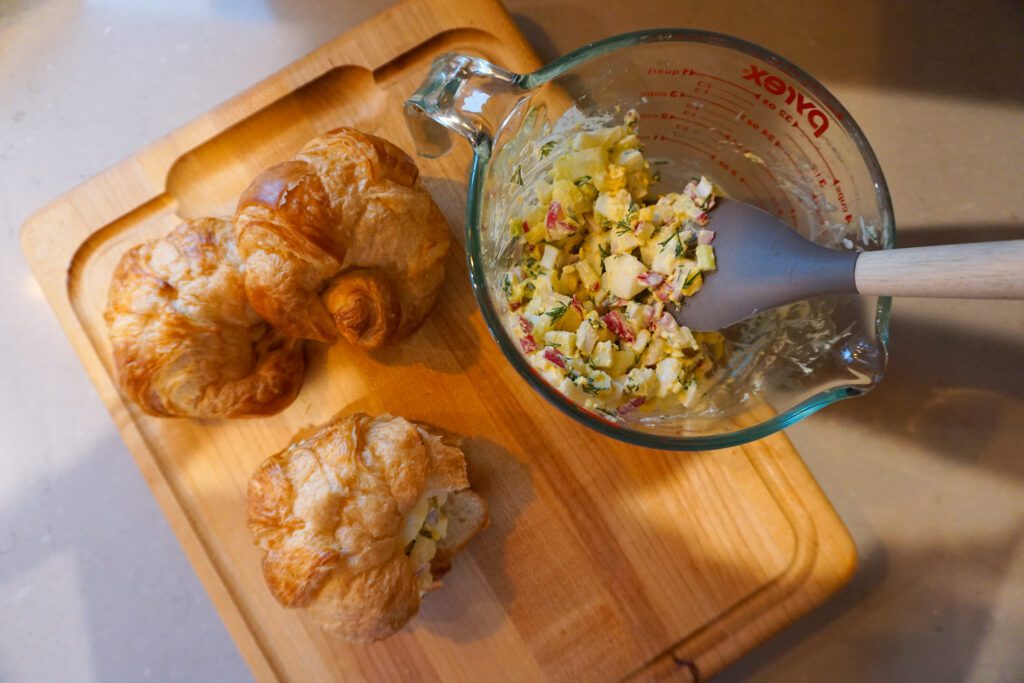 egg salad croissant sandwiches on wooden cutting board