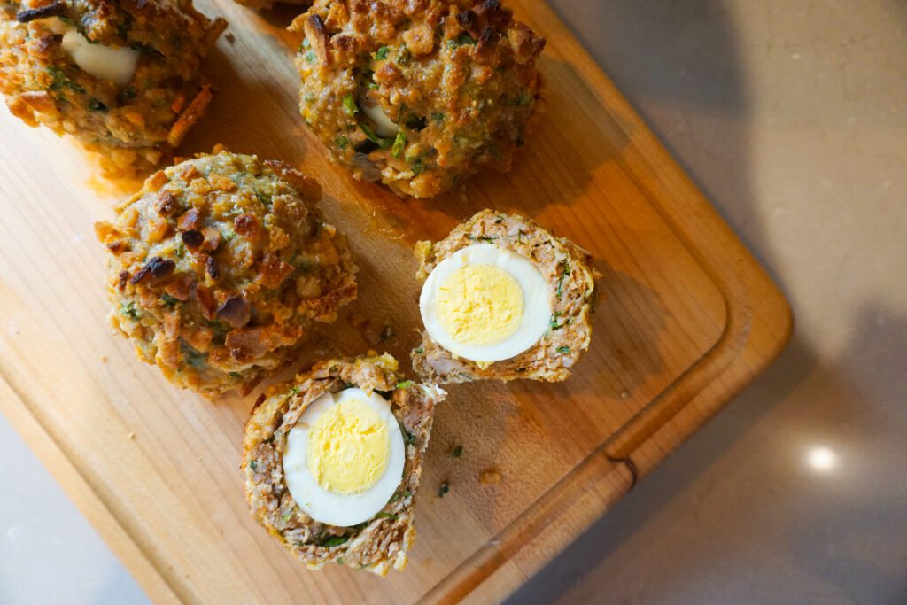 sausage wrapped hard boiled eggs, scotch eggs, cut open on wooden cutting board