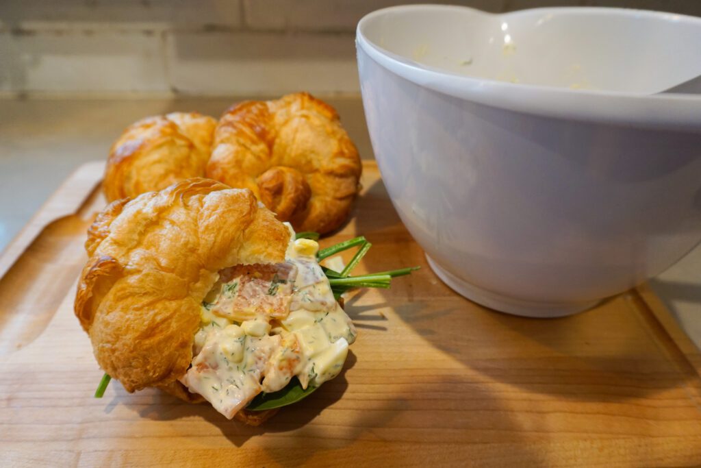 smoked salmon egg salad croissant sandwiches on wooden cutting board with white mixing bowl