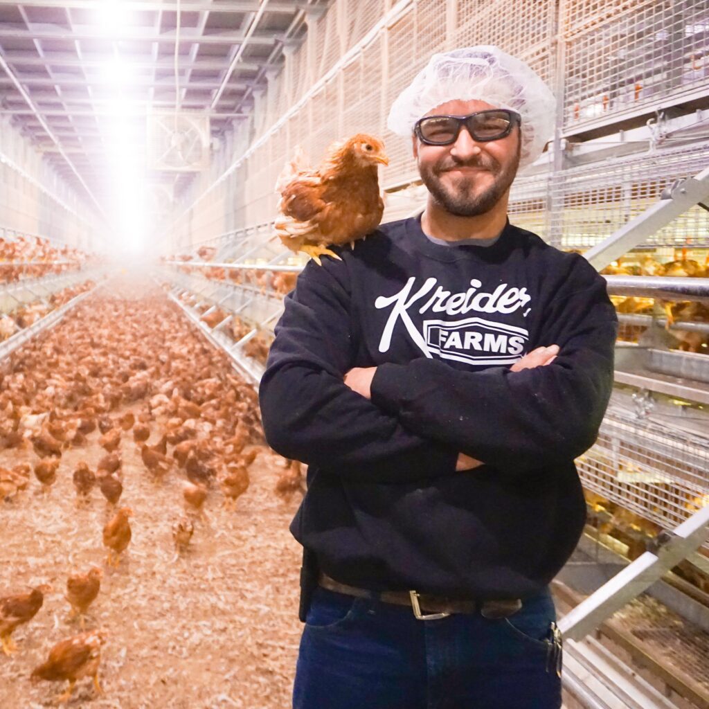 man with brown chicken on his shoulder in cage free chicken house