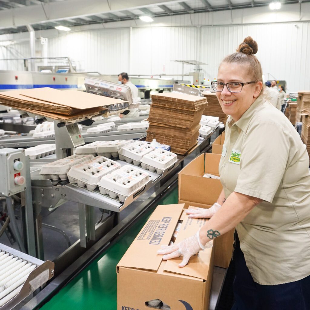 woman smiling and closing egg box in processing facility